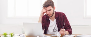 Young man sitting at desk in front of laptop, frustrated that he doesn't know how to file an amended tax return.