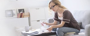 Young woman sitting at table in living room, looking through paperwork she needs to file an amended tax return.