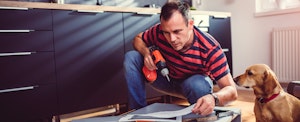 Man working on his kitchen with a drill as his dog watches