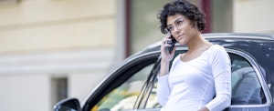 Woman leaning on her car and making a phone call