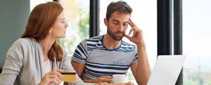 Stressed couple sitting at kitchen table and paying bills