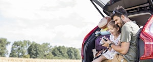 Father and daughter sitting in the trunk of their SUV during a break in their road trip