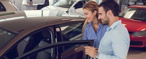 Smiling young couple looking for a new car to buy at car showroom.