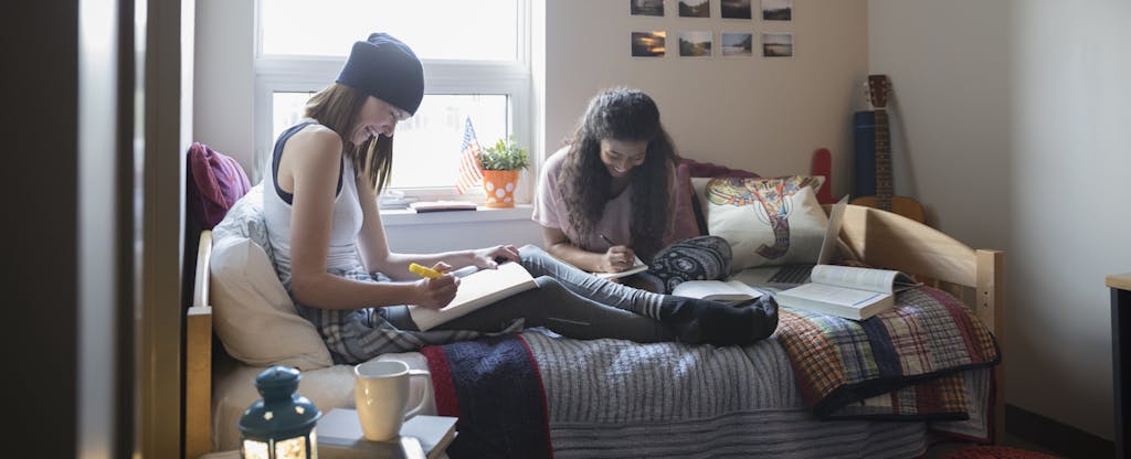 Female college students studying on bed in dorm room, wondering what kind of financial milestones they need to pass before they graduate.