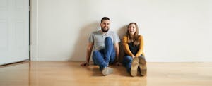 A smiling man and woman sit on the floor of their new home.