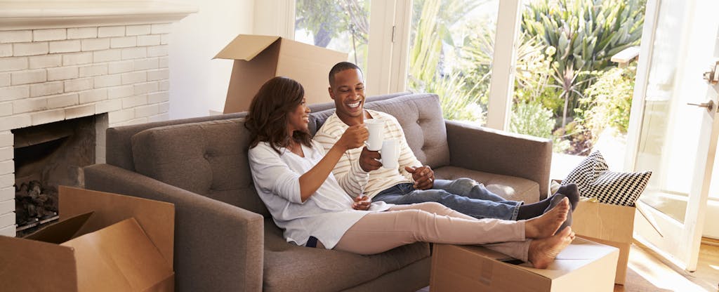 Couple On Sofa Taking A Break From Unpacking On Moving Day. They already figured out how big their down payment had to be.