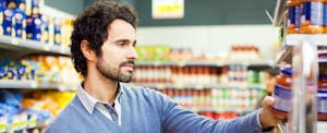 Man in a grocery store holding a jar and mentally comparing the 7 best credit cards for groceries