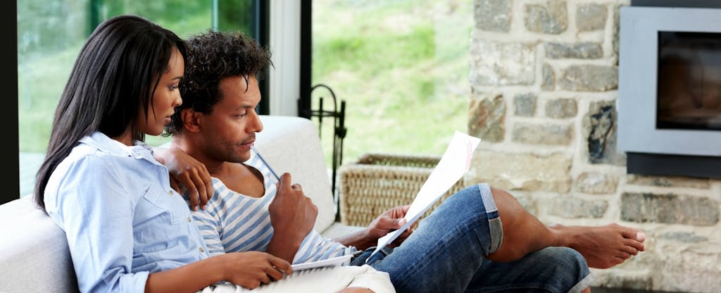 Young couple sitting in their living room and reading about the steps to build a solid financial foundation