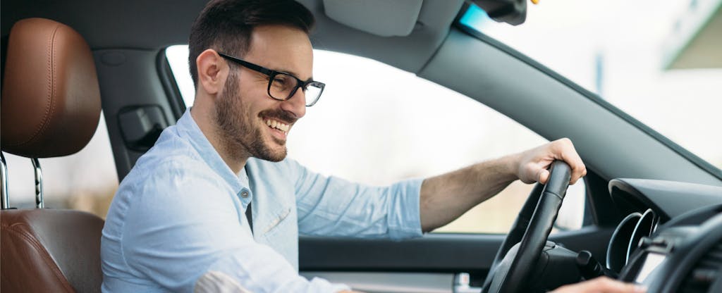Smiling man in a rental car, happy because he learned how to get car rental insurance from your credit card