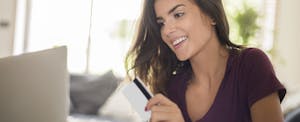 Young woman holding a credit card and looking at a laptop to learn how to find and understand your credit card CVV number