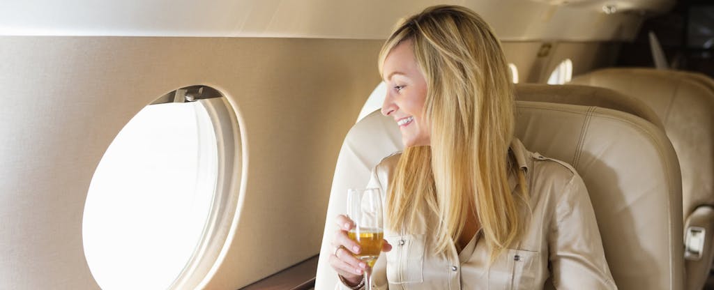Young woman sitting in first class on an airplane and smiling because she knows that the 5 most exclusive credit cards are