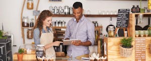 A man and a woman behind a coffee shop counter looking at a tablet to learn about the best business credit cards for business owners and entrepreneurs
