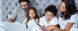 Young family sitting in bed, gathered around a laptop to learn what you need to know about credit card companies