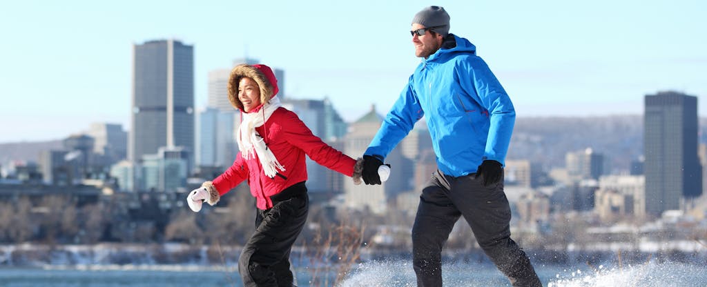 Young couple in winter gear running through a park with a cityscape in the background as they discuss the best PNC Bank credit cards