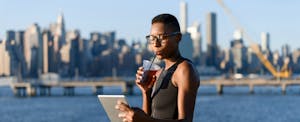 Woman on a boardwalk, sipping a cold drink, and using the best ways to send money transfers online on her tablet