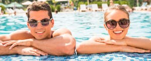 Young couple hanging off the edge of a pool and smiling because they compared platinum american express, chase sapphire reserve, and the citi prestige and ended up with the best card for them.