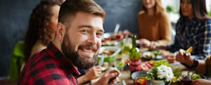 Young man at a festive dinner with friends, smiling because he finally settled the Chase Freedom vs. Chase Freedom Unlimited vs. Discover it debate