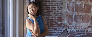 Woman looking out a window while leaning against a brick wall while wondering when credit card companies report to credit report bureaus