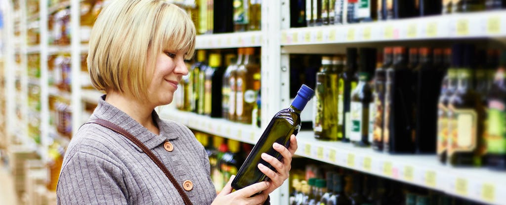 Woman shopping in a grocery store, considering purchasing a bottle of wine
