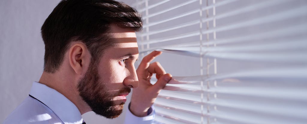 Man looking out a window with suspicion, wondering how hackers are going to use his stolen information