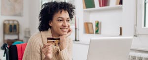 Woman smiling at laptop and holding her credit card while online shopping.