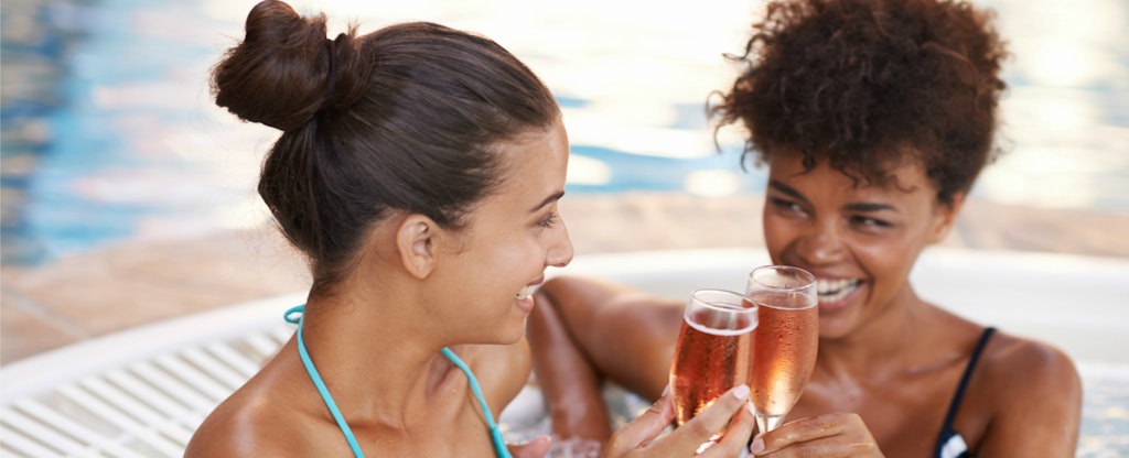 Two friends toasting each other with prosecco in a hot tub