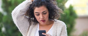 Concerned young woman looking at her phone to figure out what 5 things to do if you spot an unauthorized credit inquiry.