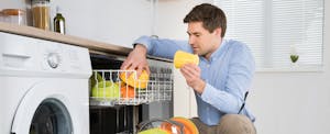 Man crouching to unload a dishwasher while wondering how to deal with delinquent accounts.