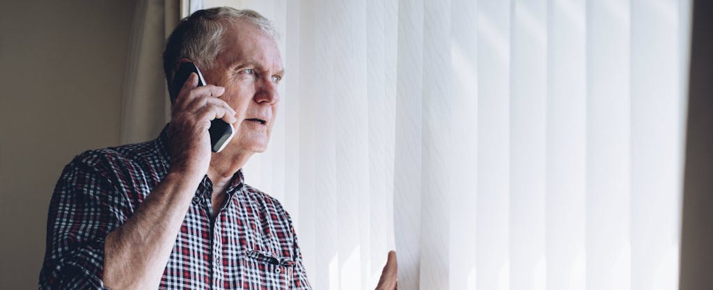 Senior man peering out the window and asking someone on the phone what to do if you're a victim of credit card fraud