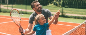 Dad teaching his daughter how to play tennis after buying her a racket using a Dick's Sporting Goods credit card