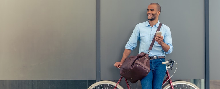 Man standing alongside his bicycle, listening to music on his phone and smiling