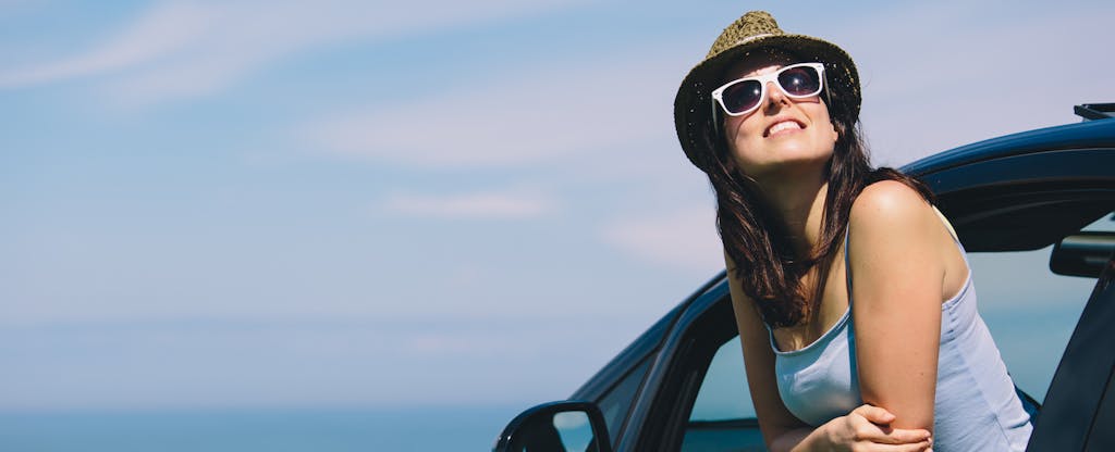 Young woman leaning out of her car window and thinking about whether or not it's worth it to refinance an auto loan
