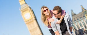 Young couple on vacation, fooling around in front of Big Ben after learning about the 9 airlines that offer companion tickets or discount codes