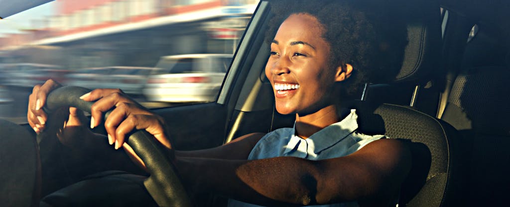 Smiling woman driving a car and wondering how often to shop for car insurance