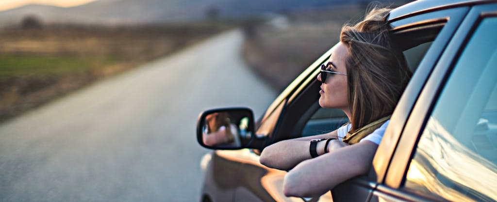 A woman in a car at sunset contemplates her potential auto refinancing savings