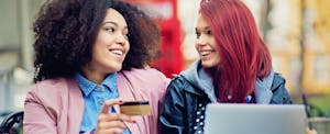 Two friends are shopping online with their new Total Visa credit card, an unsecured card for applicants with poor credit.