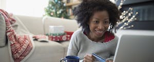 Smiling woman with credit card online shopping at her home decorated with holiday cheer, happy that she's using her credit card rewards to help her pay for gifts and avoid holiday debt