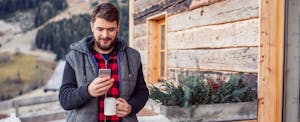 Young man drinking coffee outdoors and using his phone to check his tax refund status