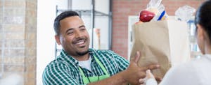 Young African-American business owner hands a bag of groceries to a food bank volunteer.