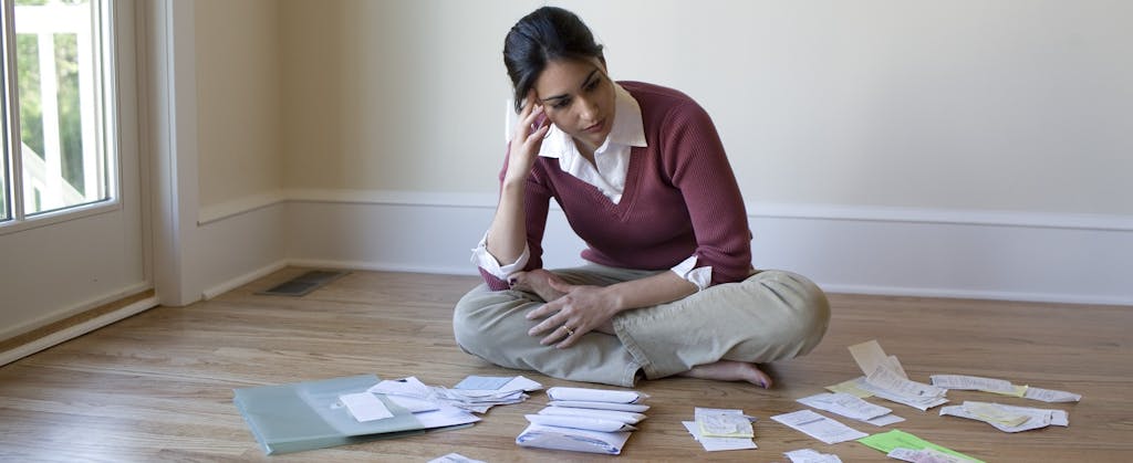 Woman sitting on floor, looking at bills and receipts