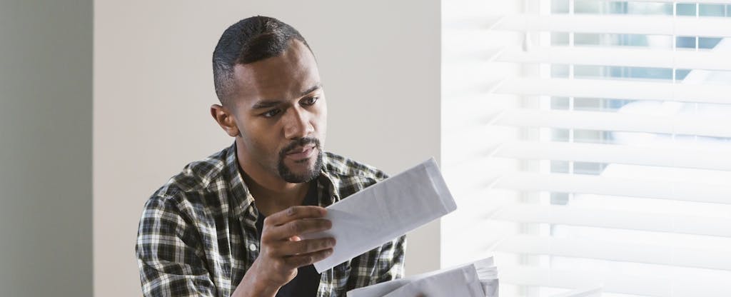 Young African-American man sorting through mail and looking for his income tax refund check.