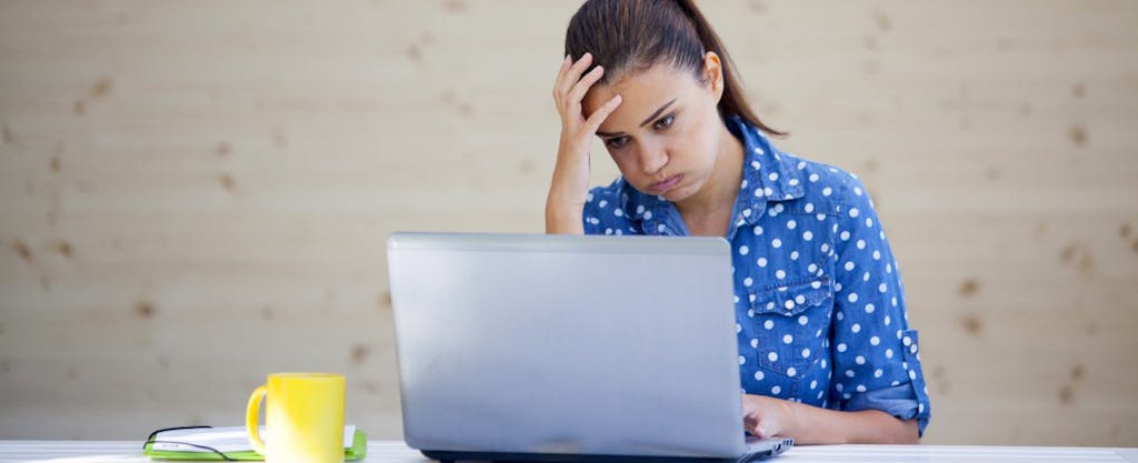Young woman working on laptop, frustrated by common tax filing mistakes on her income tax return.