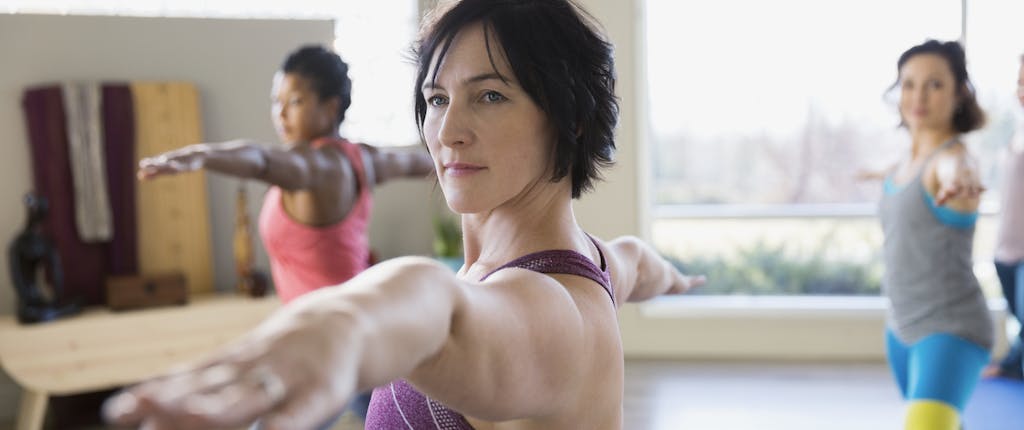 A woman in a yoga class gazes ahead while holding the warrior II position.