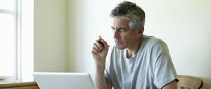 A man with gray hair holds a pen and studies his laptop, wondering what happens when you file bankruptcy.