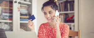 Credit card in hand, young woman works at home.