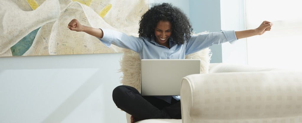 African-American woman sitting on couch and cheering expired tax breaks that have been extended.