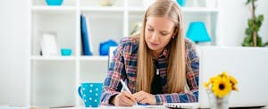 Young woman sitting at a desk, reviewing tax preparation documents needed for filing your own taxes