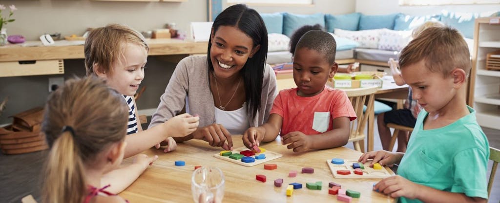 Smiling young teacher teaching children about letters and shapes in daycare.