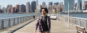 Young man in hat walking and laughing against New York City skyline
