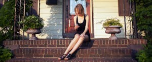 Young woman sitting on the front porch of her home, using her mobile phone to look up what is a tax lien.